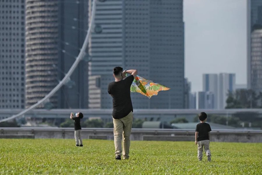 A father flying a kite with two children on a grass field