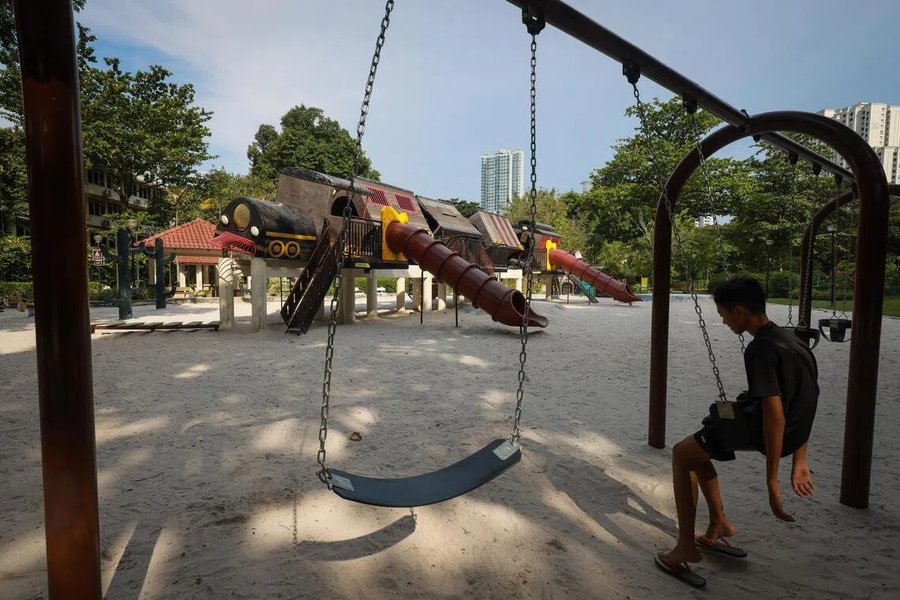 A boy on a swing beside the tilting train playground in Tiong Bahru Park