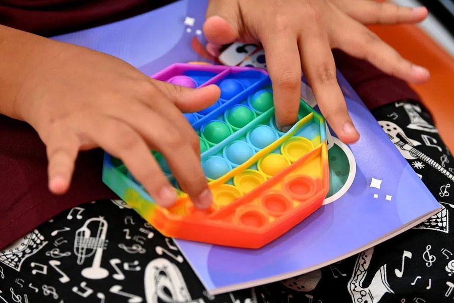 A child's hands playing with a pop-it fidget toy on a notebook